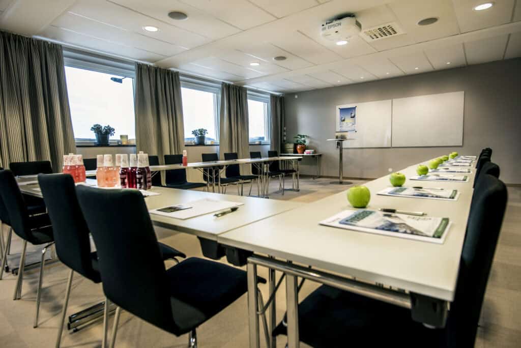 Främre bild av ett modernt konferensrum i Funäsdalen med stora fönster, gröna äpplen och konferensmaterial för effektiva fjällresor och fjällsemester.